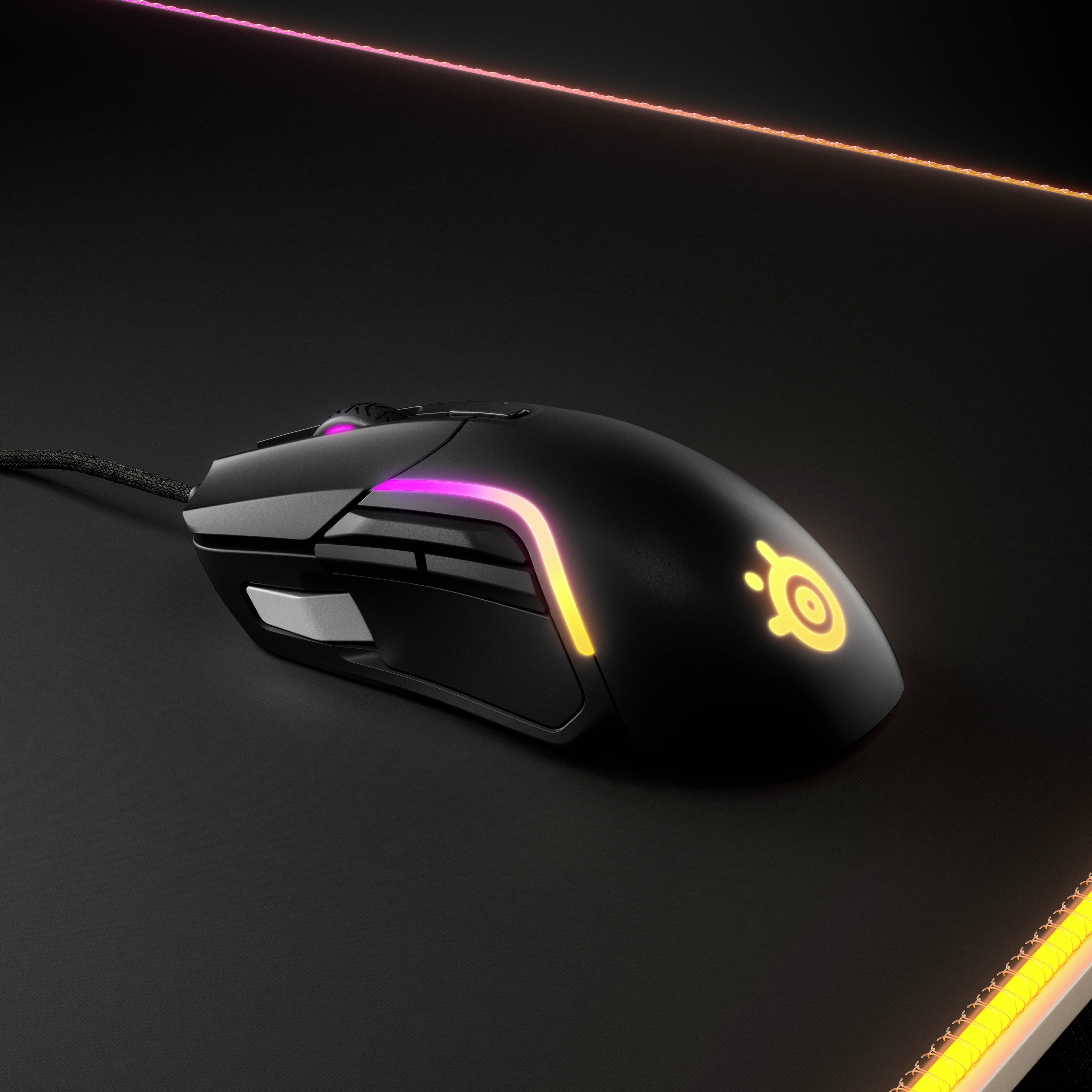Une souris de gaming noire avec éclairage RVB sur un tapis de souris sombre, illuminée de différentes couleurs.