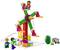 Plusieurs personnages jouent avec un grand ensemble de manège en Lego coloré. Un petit tracteur de jouet et des plantes sont également visibles.