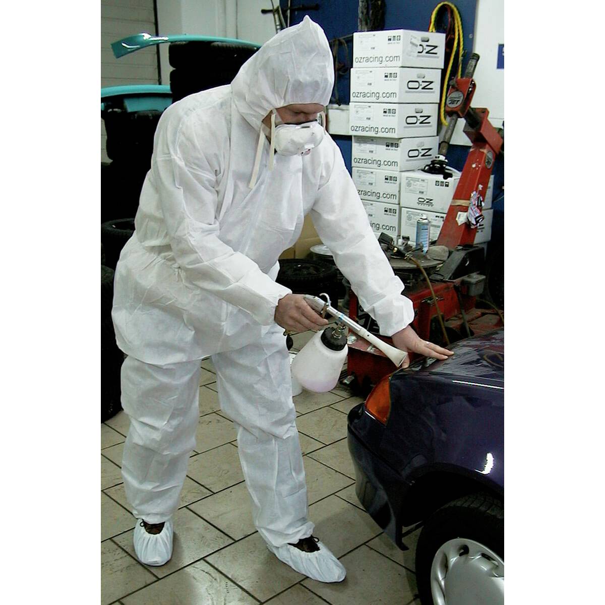 Une personne en combinaison de protection peint une voiture dans un atelier.