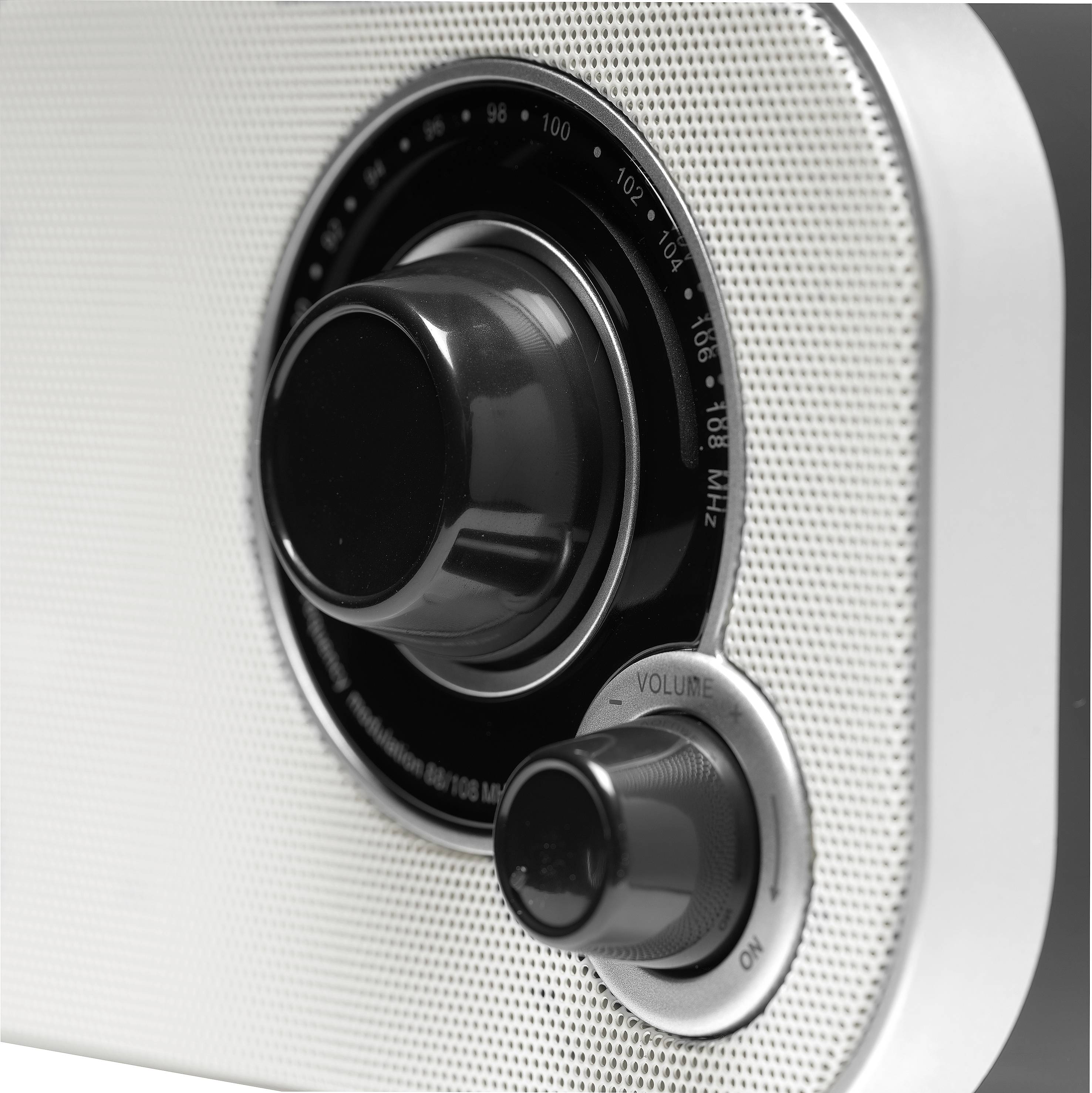 Gros plan d'un poste de radio rétro avec de grands boutons rotatifs pour la fréquence et le volume, posé sur une surface métallique.