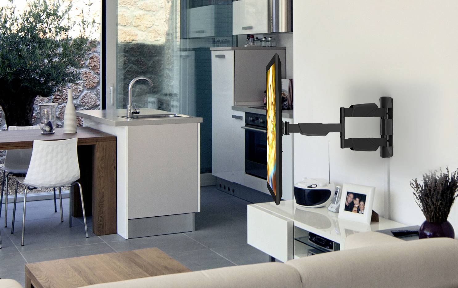 Un espace de vie moderne et ouvert avec une cuisine en arrière-plan et un support mural qui maintient un téléviseur à écran plat au-dessus d'une table en verre.