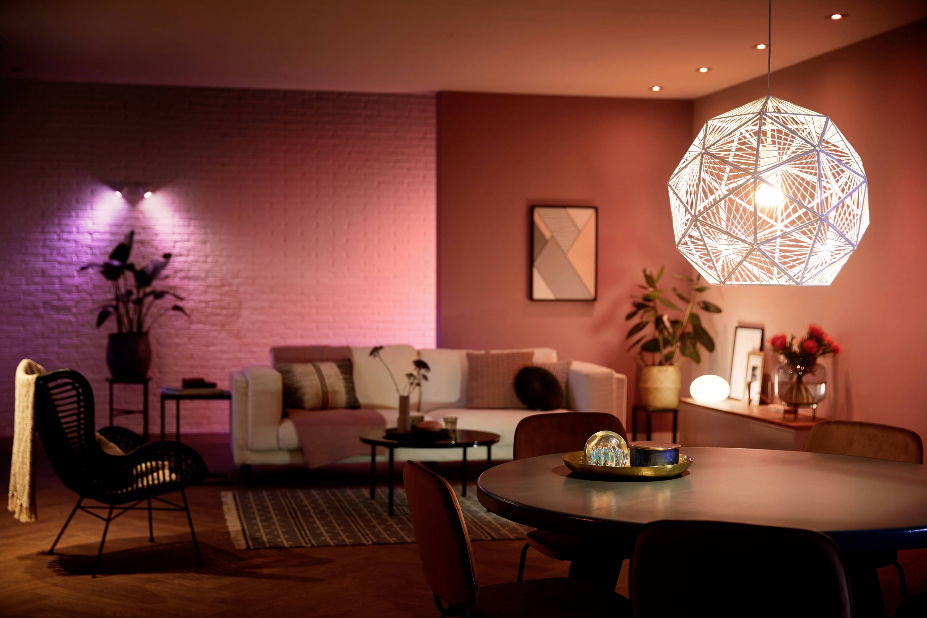 Un salon au design moderne avec une table ronde au premier plan. Une suspension géométrique éclaire la pièce.