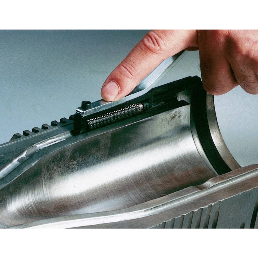 Gros plan d'une main inspectant une coupure dans un tuyau métallique. Un tournevis et une vis sont visibles.