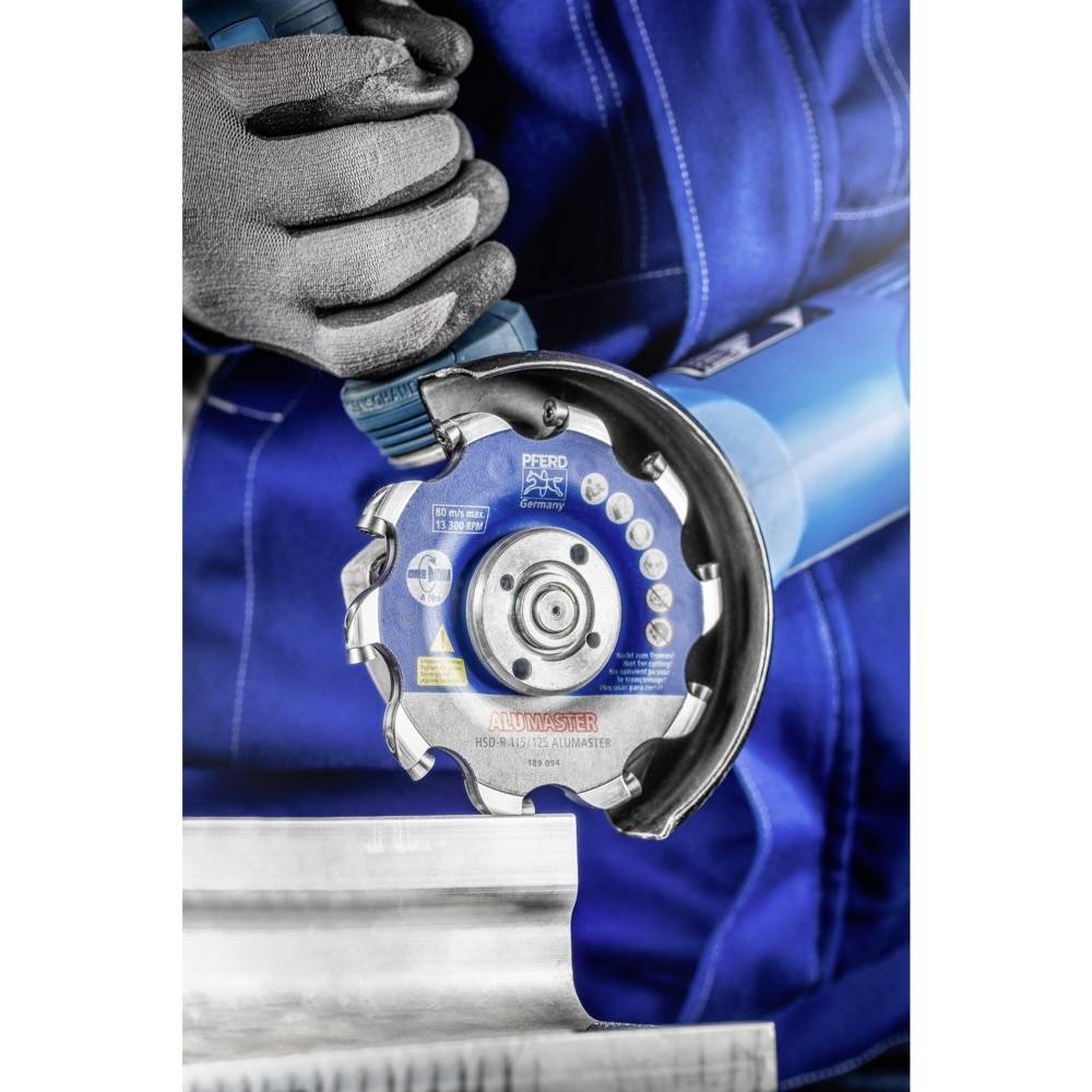 Un ouvrier vêtu d'un équipement de protection bleu tient une meuleuse contre une pièce métallique. La machine porte des certificats de sécurité.