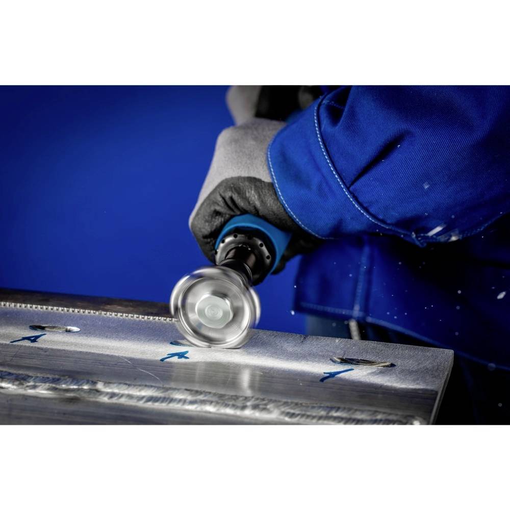 Une personne vêtue de vêtements de travail bleus et portant des gants travaille avec une meuleuse sur une surface métallique.