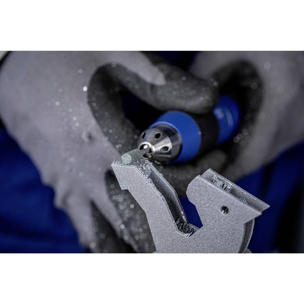 Une personne tient un outil bleu en rotation, portant des gants de protection gris. L'outil travaille le bord d'un objet métallique.