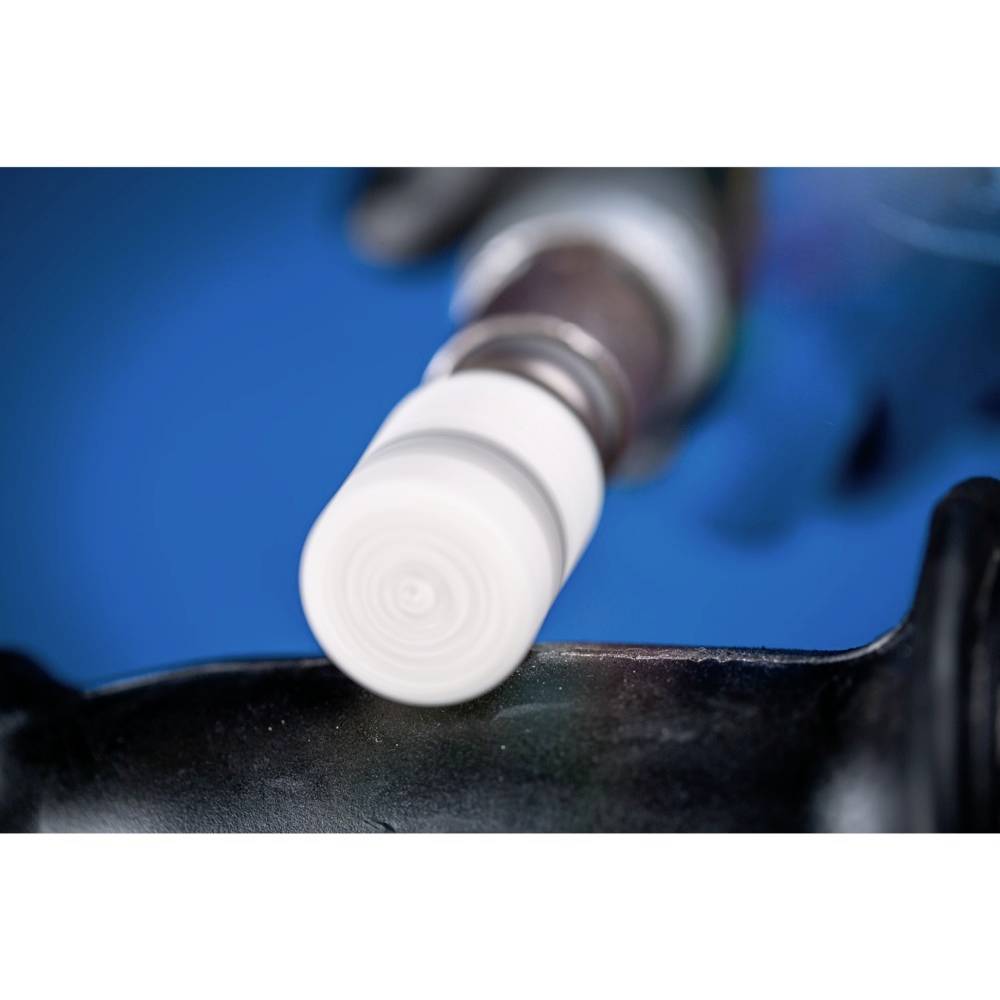 Gros plan d'un appareil avec un embout blanc en action, sur un fond bleu flou. Mise au point principale sur l'embout et sa structure.