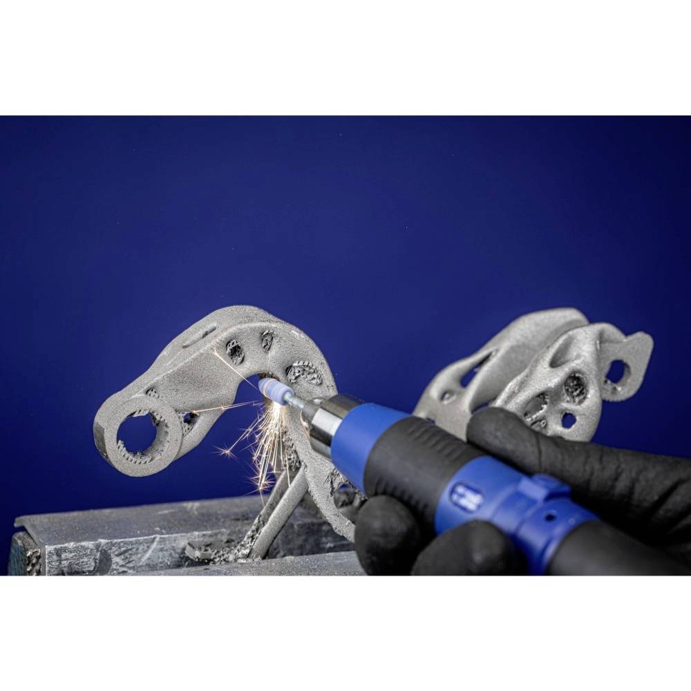 Une main gantée de noir utilise un outil pour travailler des pièces métalliques. Des étincelles volent au point de contact.