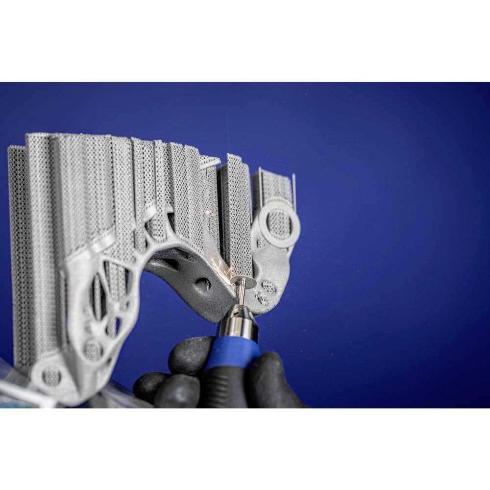 Une personne portant des gants noirs manipule une pièce métallique complexe à l'aide d'un outil bleu sur un fond bleu.