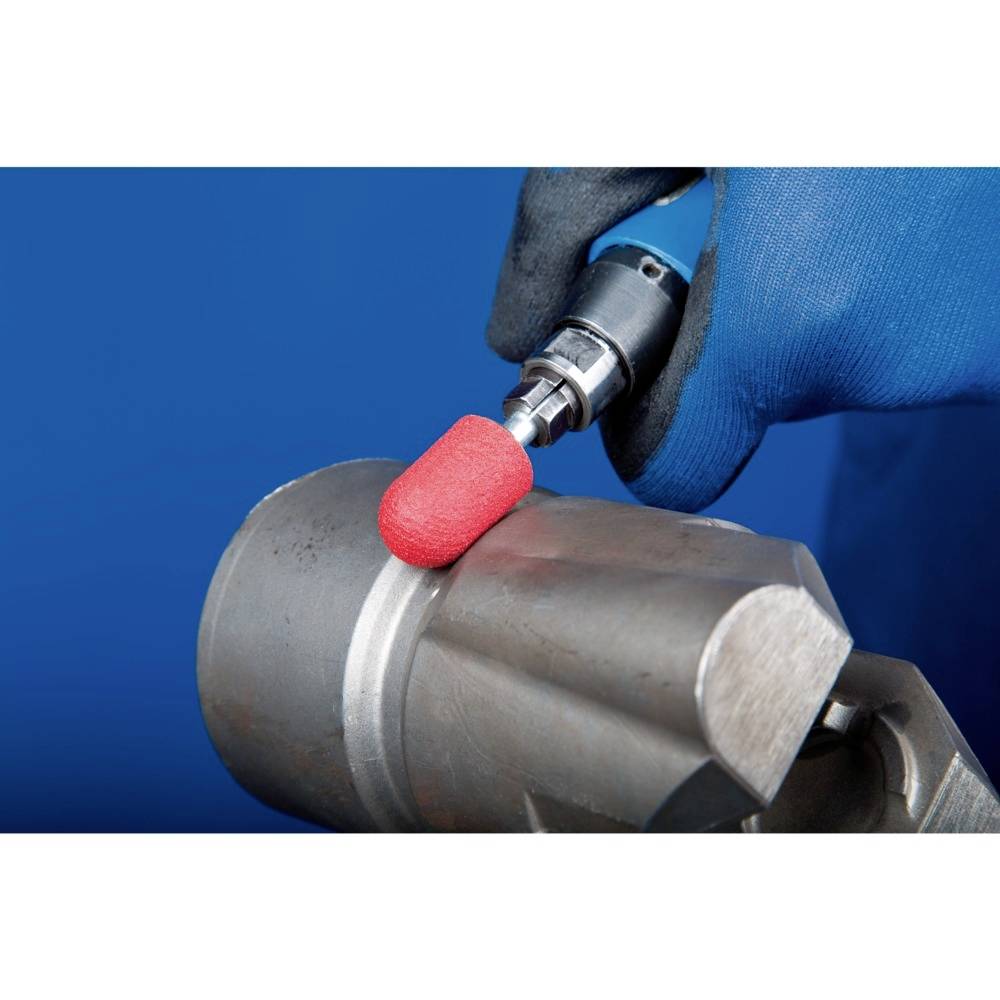 Une personne travaille une pièce métallique avec un embout de meulage rotatif. Une main porte un gant de travail bleu.