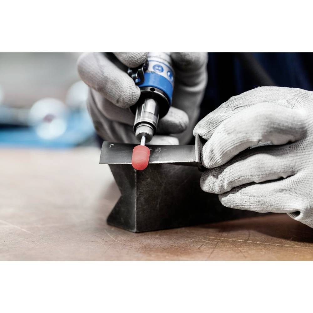 Une personne portant des gants polit un morceau de métal à l'aide d'une machine-outil rotative. L'arrière-plan est légèrement flou.