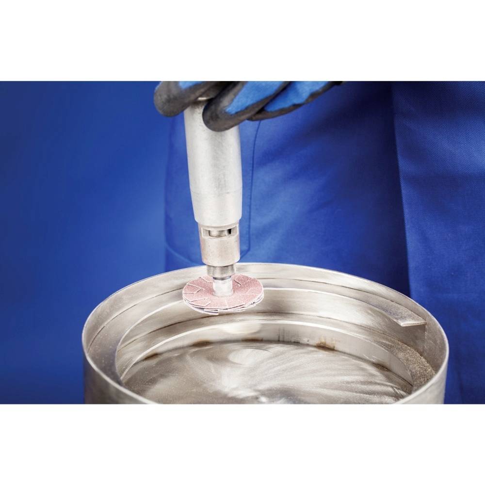 Gros plan sur un processus de production : Une personne portant des gants bleus utilise un outil rotatif sur une plaque métallique.