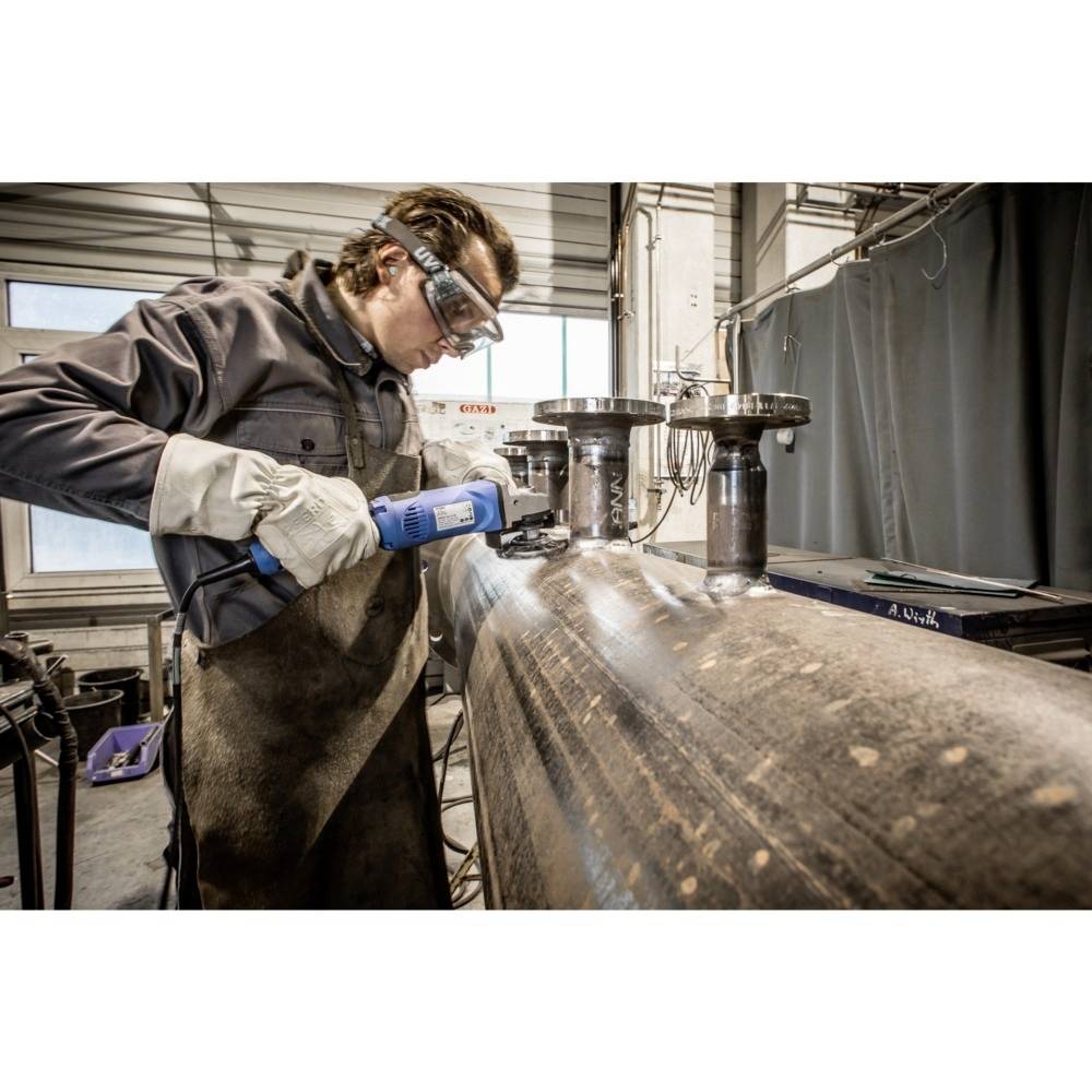 Un homme portant des lunettes de protection et des gants meule un tube métallique dans un atelier.