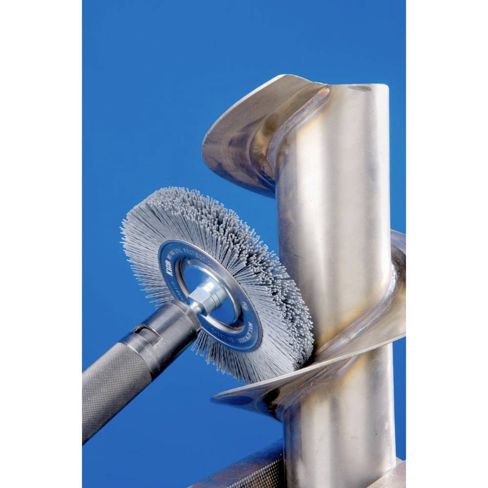 Un meuleuse d'angle équipée d'une brosse métallique polit un raccord de tuyauterie. La brosse enlève du matériau pour lisser la surface.