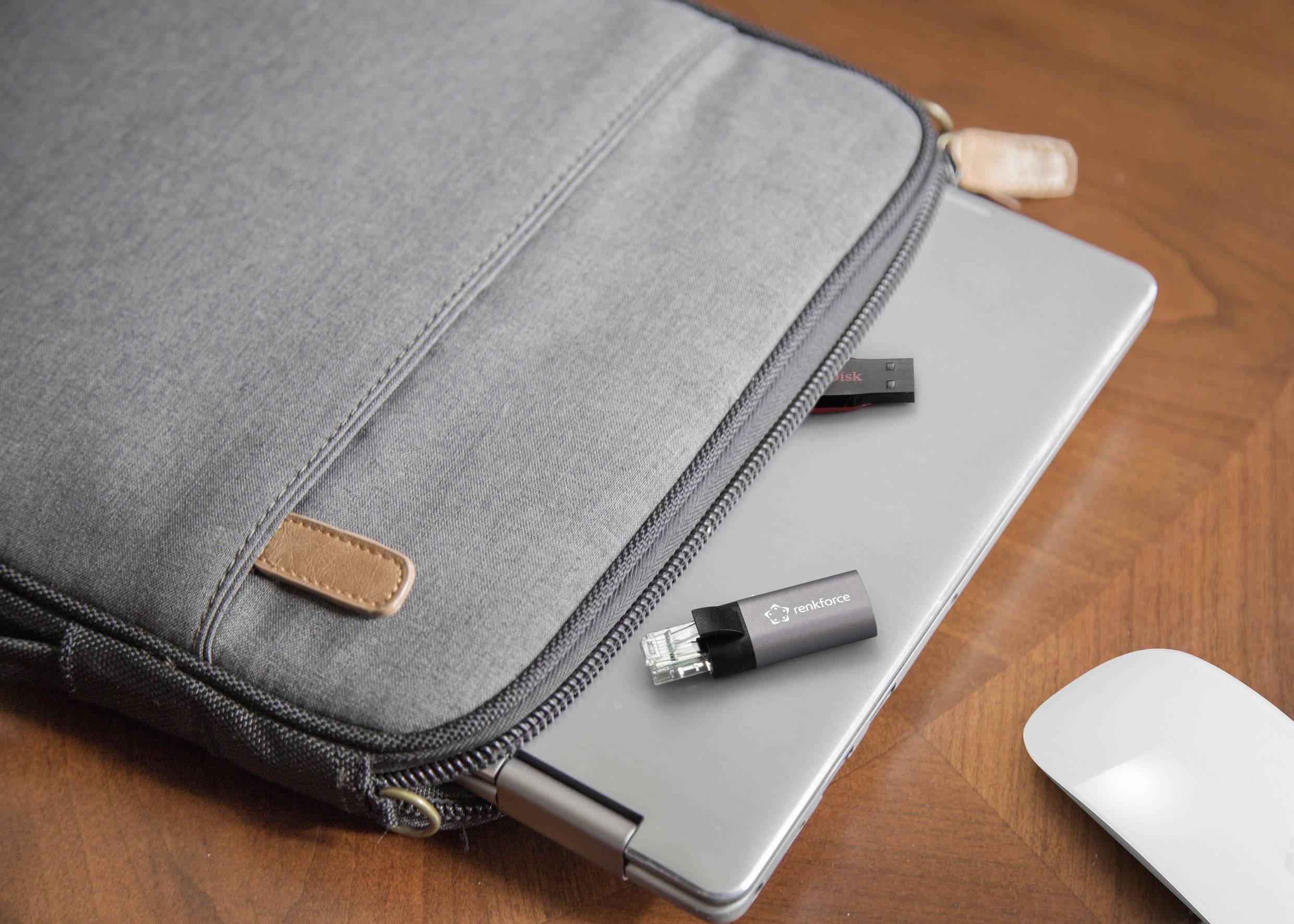 Un ordinateur portable gris dépasse à moitié d'un sac en tissu gris posé sur une table en bois. À côté de l'ordinateur portable, deux clés USB sont disposées.