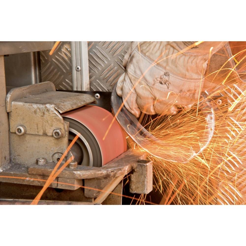 Une personne meule du métal sur une machine, des étincelles jaillissent. Des gants de protection sont portés, la sécurité au travail est importante.