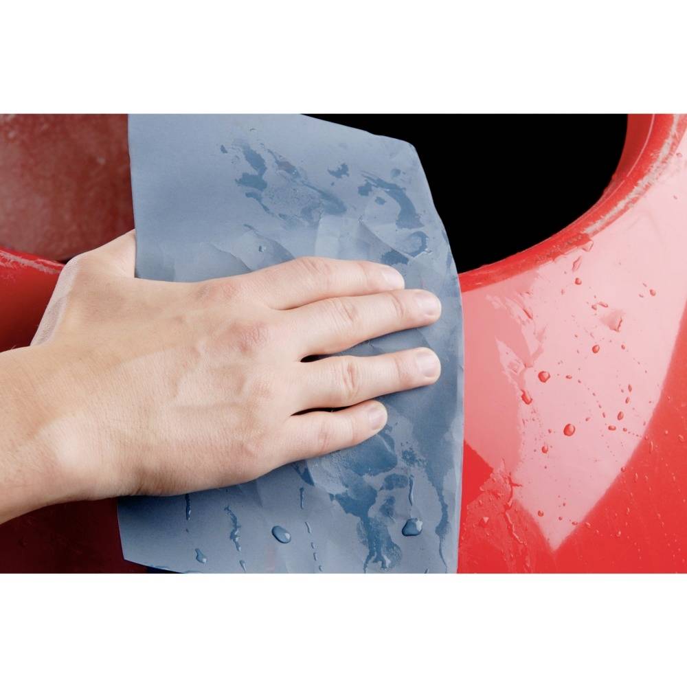 Une main essuie de l'eau avec un chiffon bleu sur une surface rouge et brillante.