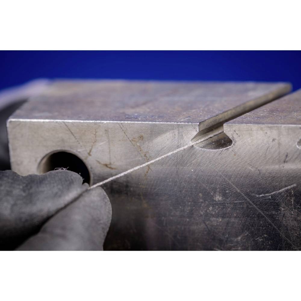 Gros plan sur une main manipulant une fine scie pour travailler une pièce métallique délicate, dans un environnement d'atelier.