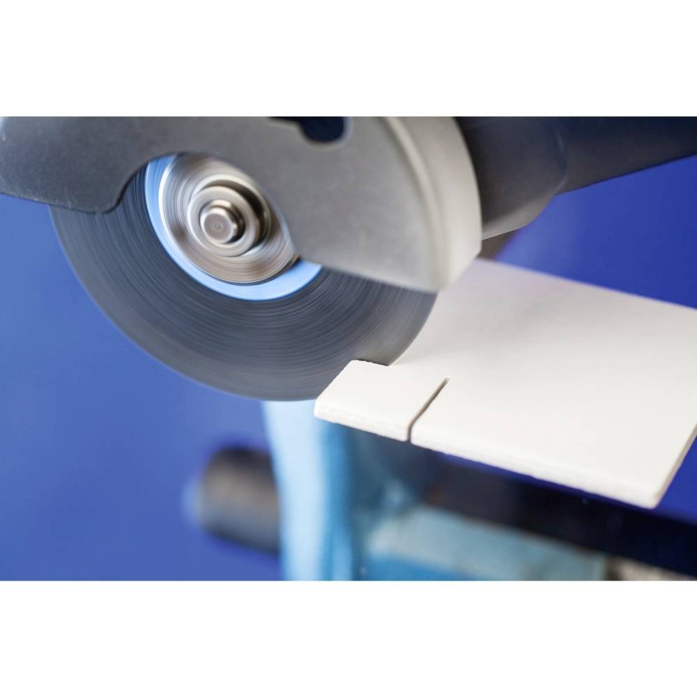 Une machine coupe un matériau de carrelage blanc à l'aide d'une lame rotative sur un fond bleu.