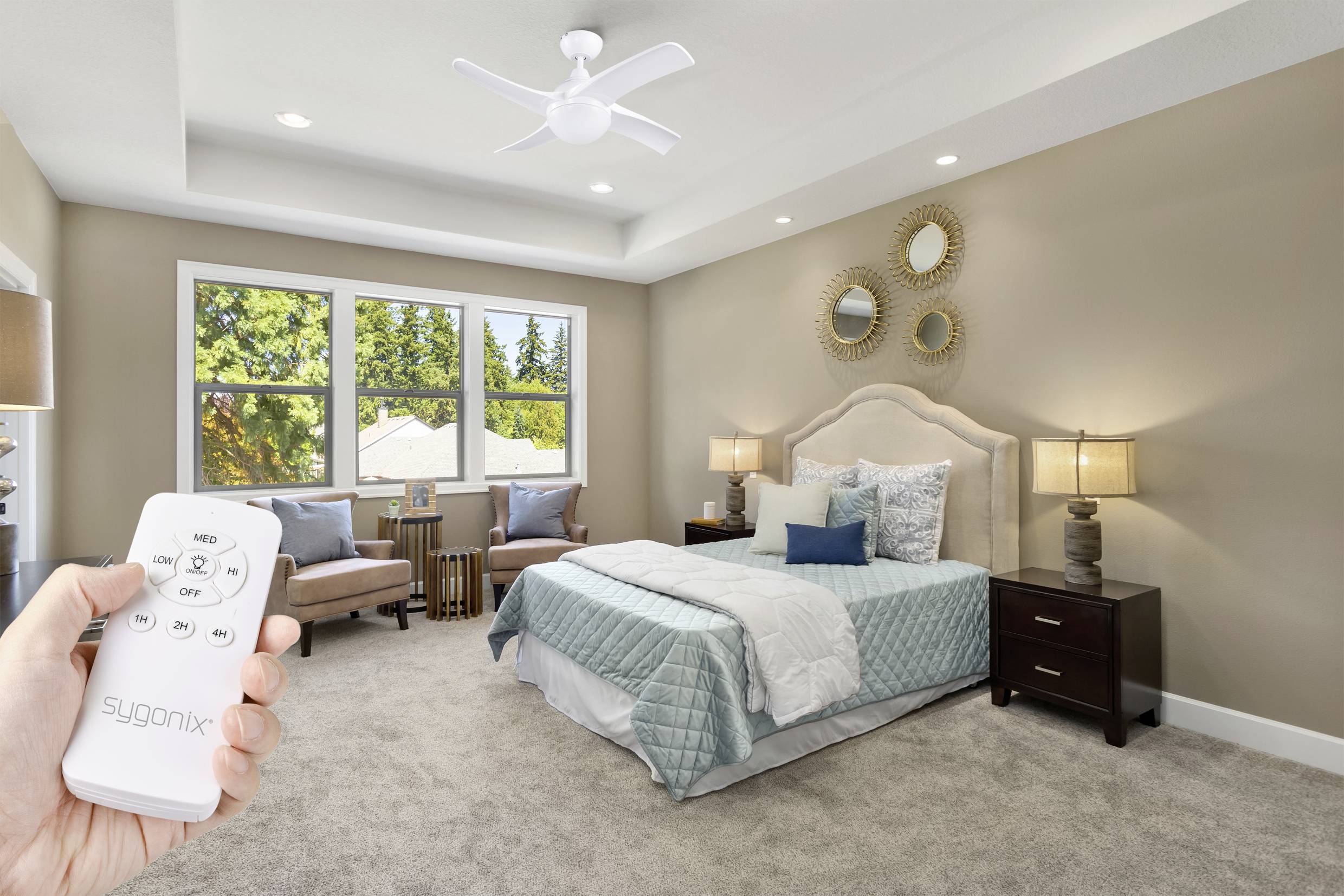 Une chambre aux murs clairs, avec un lit au centre et une personne tenant une télécommande pour le ventilateur de plafond.