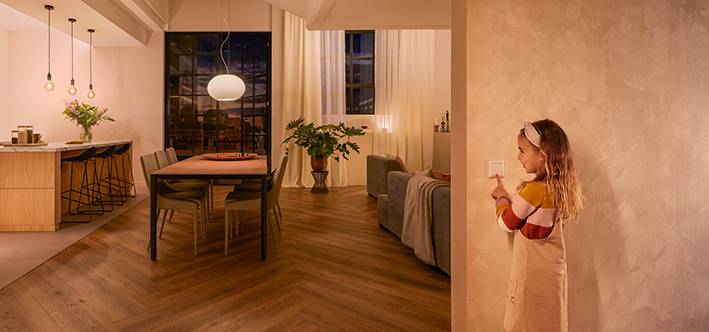 Un enfant actionne un interrupteur et illumine un espace de vie et de repas moderne et accueillant avec une lumière chaleureuse en arrière-plan.