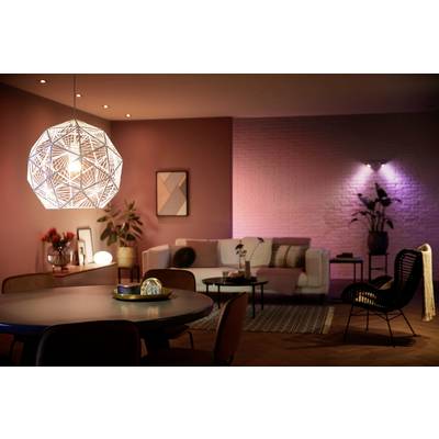 Salon confortable avec une suspension moderne, un canapé beige, des décorations et un éclairage tamisé. L'atmosphère semble accueillante.