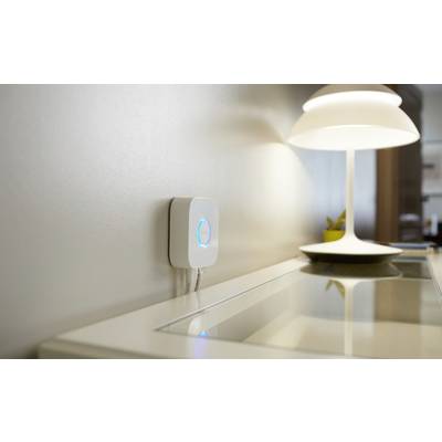 Un appareil blanc et lumineux est monté sur le mur. À côté, une lampe moderne est posée sur une table.