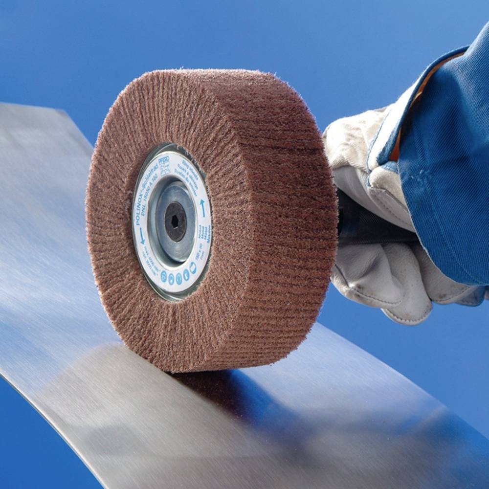 Des mains gantées polissent une pièce métallique avec une meule rotative sur un fond bleu.