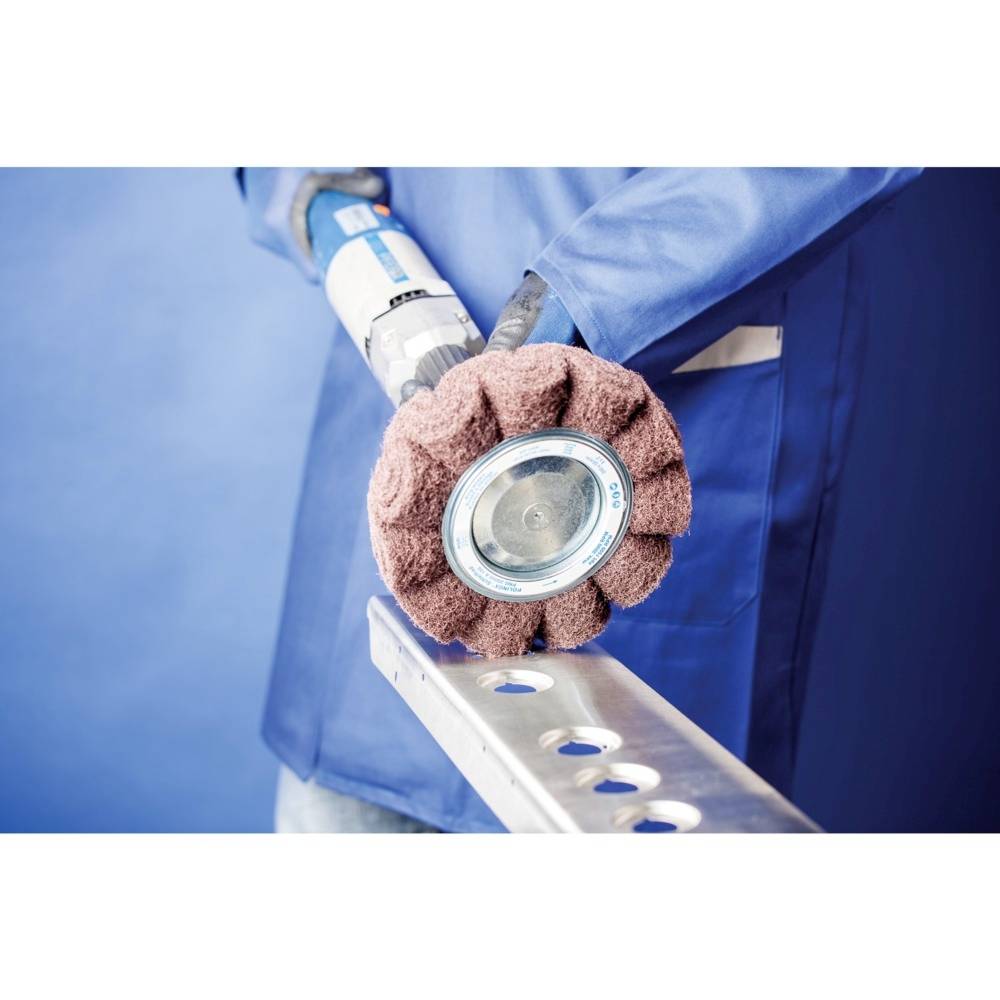 Une personne ponçe une pièce métallique avec un disque abrasif rotatif, tout en portant des vêtements de protection et des gants.