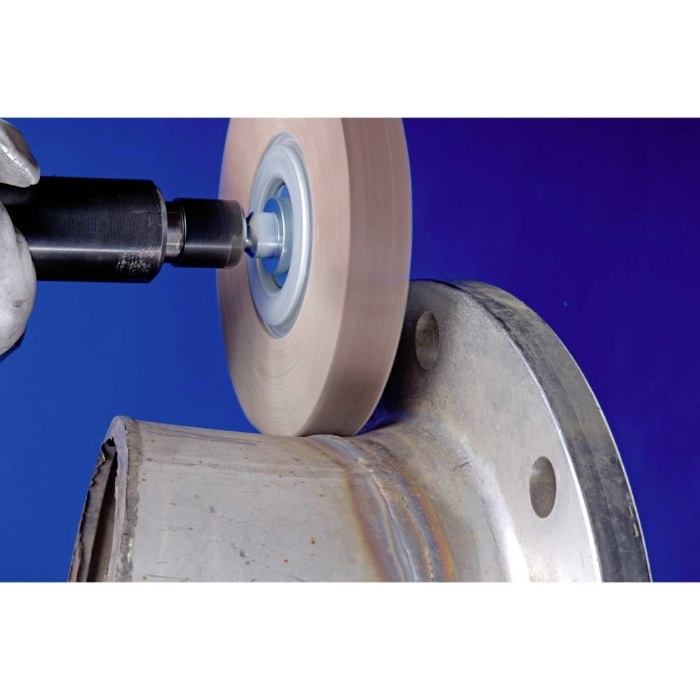 Une machine usiné une pièce métallique avec un outil de meulage rotatif. Une main tient la machine, sur un fond bleu.