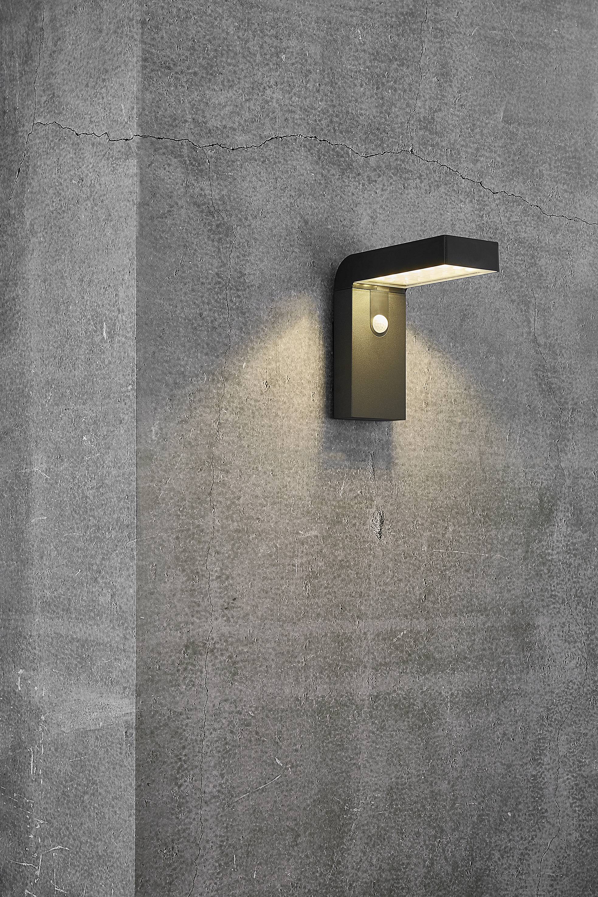 Applique murale extérieure au design moderne et rectangulaire projetant une lumière chaleureuse sur un mur en béton gris. Idéale pour une architecture contemporaine.
