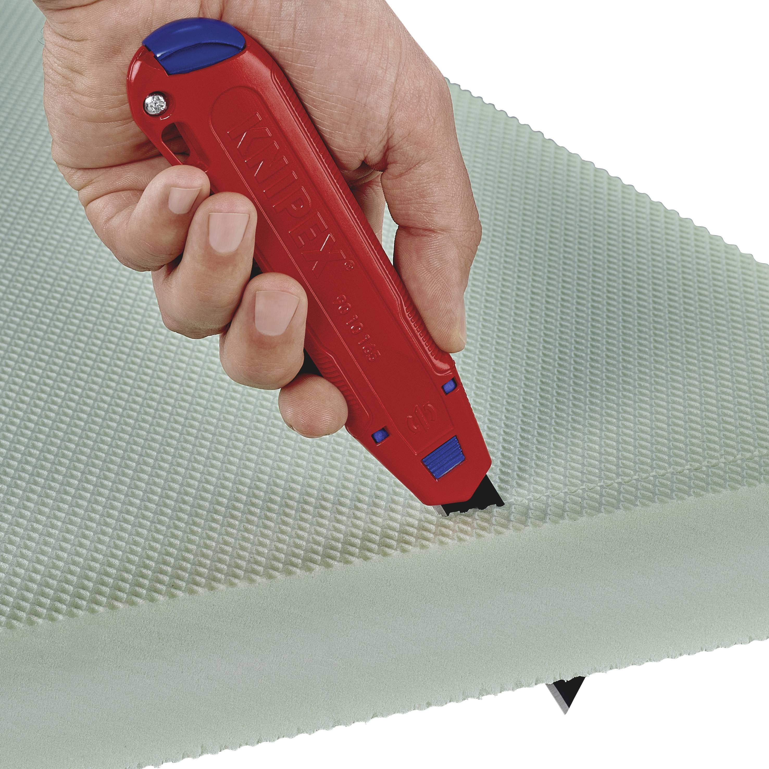 Une main tient un couteau universel rouge et coupe une plaque de mousse verte.