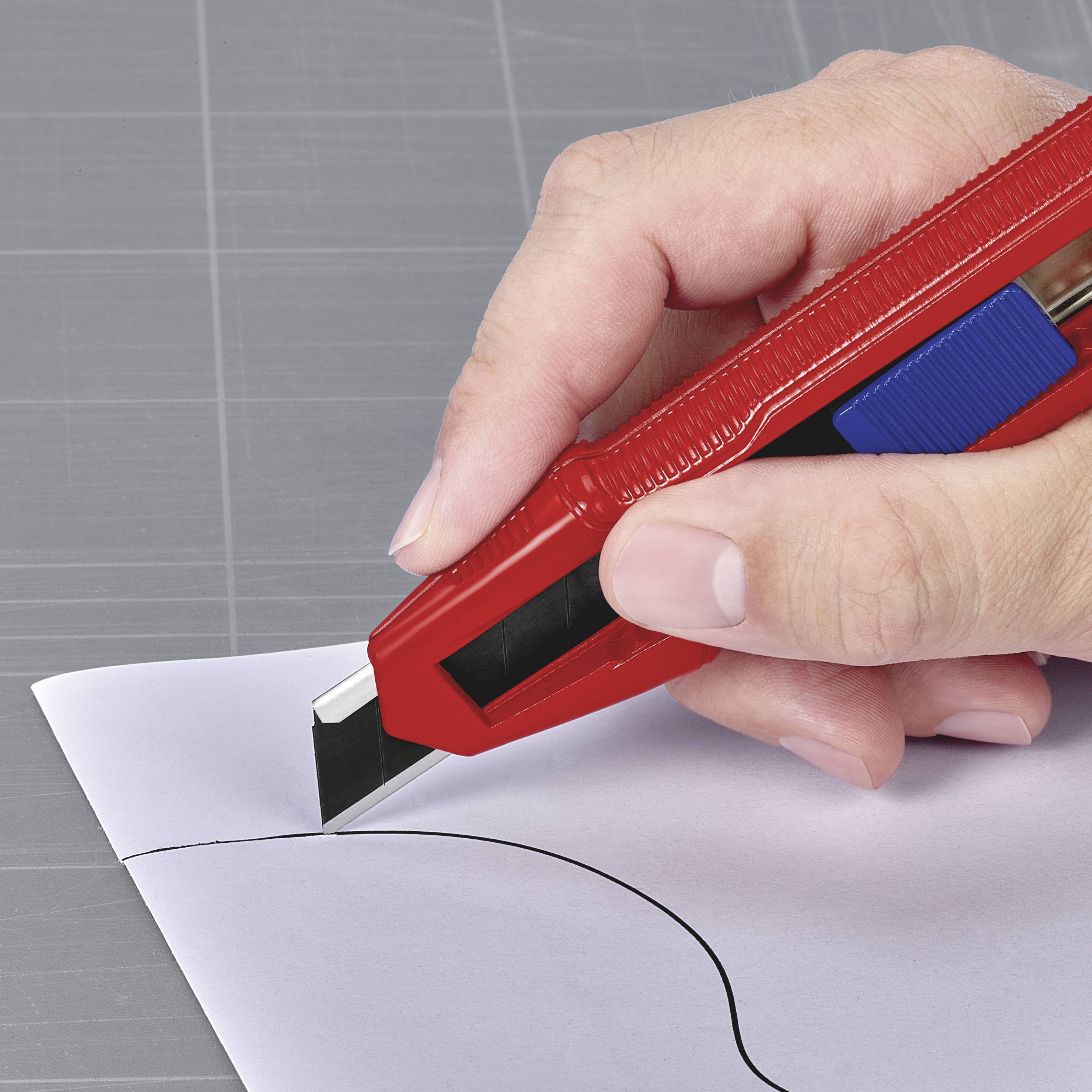 Une main tient un cutter et coupe précisément du papier le long d'une ligne noire sur une planche à découper.