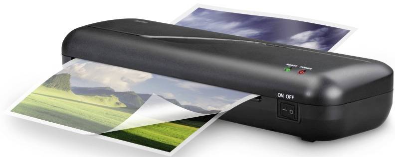 Un appareil de laminage en train de laminer une photo. La photo représente un paysage avec des prairies vertes et un ciel nuageux.