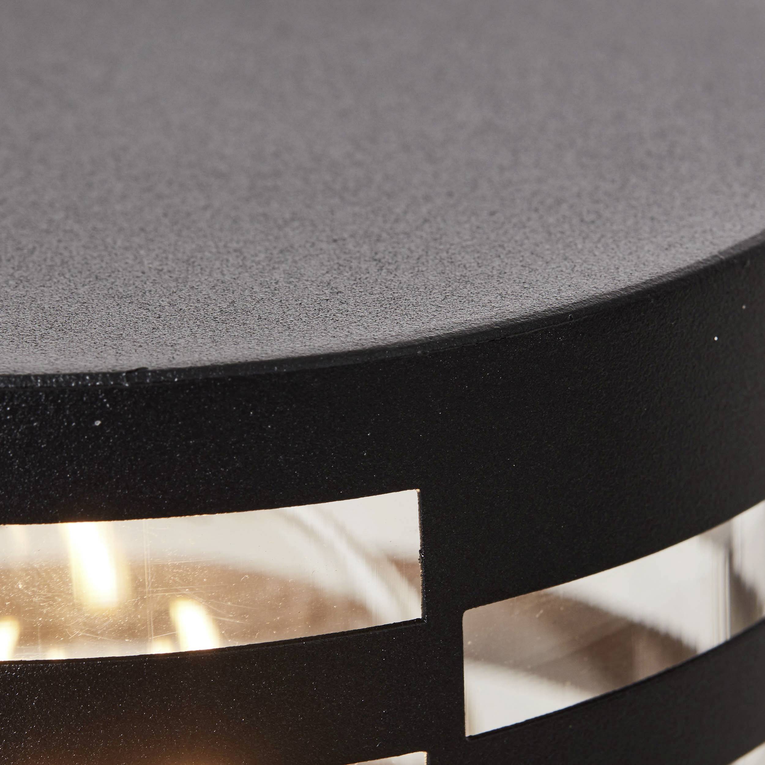 Gros plan d'une lampe moderne noire avec de la lumière visible à travers des fentes étroites. Boîtier métallique mat et brossé.