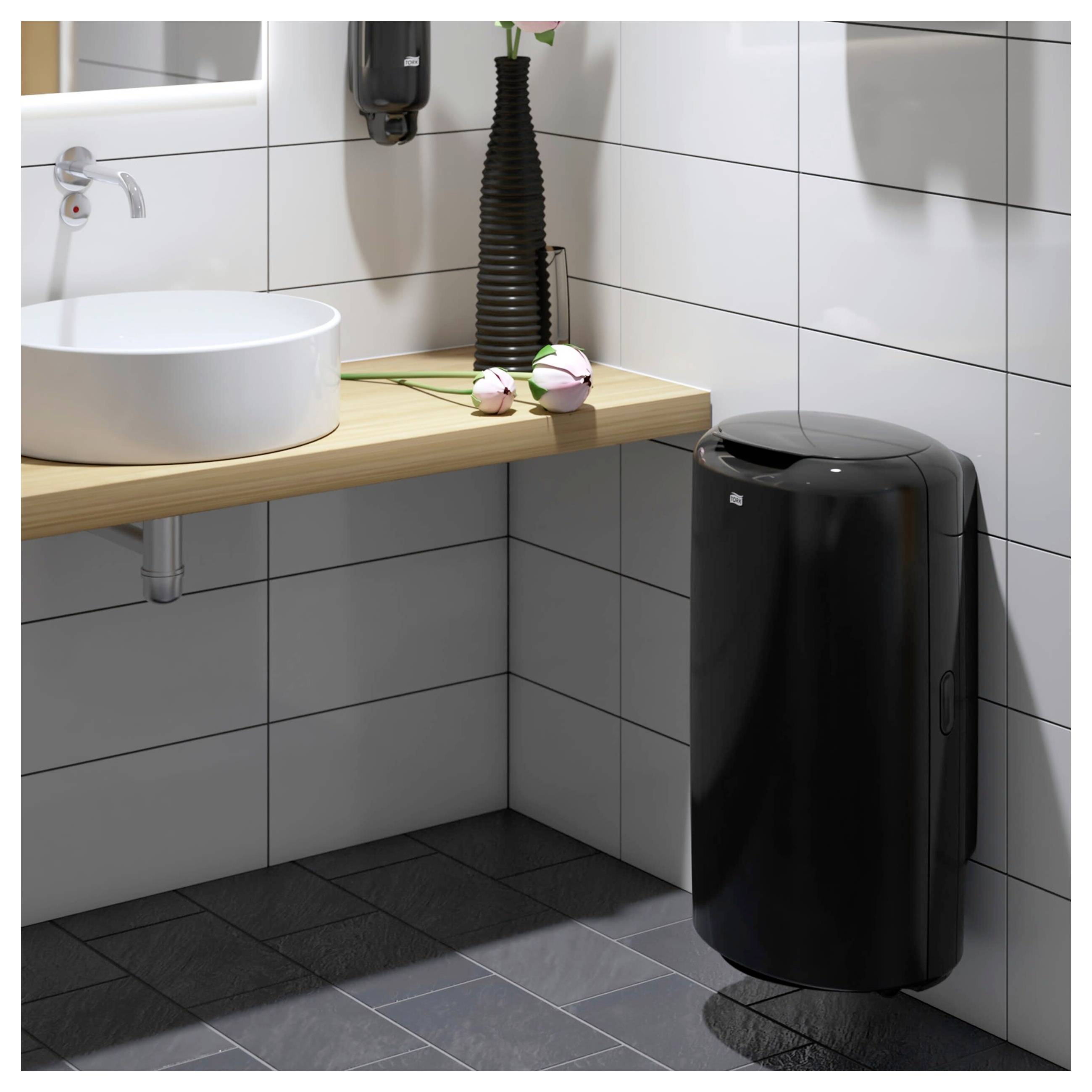 Coin de salle de bain carrelée moderne avec un lavabo blanc suspendu, un plan de travail en bois, et un distributeur de savon noir et une poubelle.