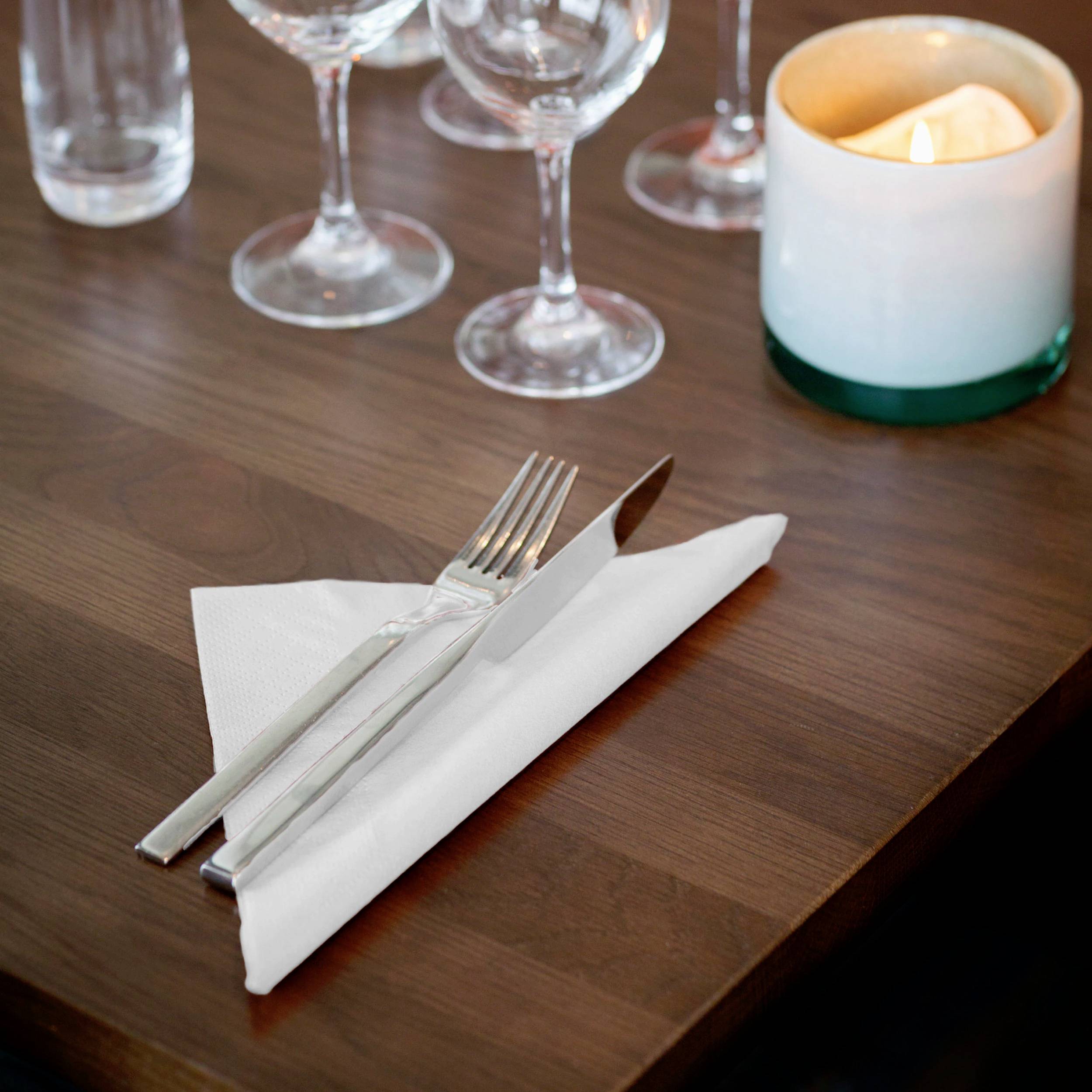 Couverts sur une serviette blanche posée sur une table, entourés de verres à vin et d'une bougie allumée.