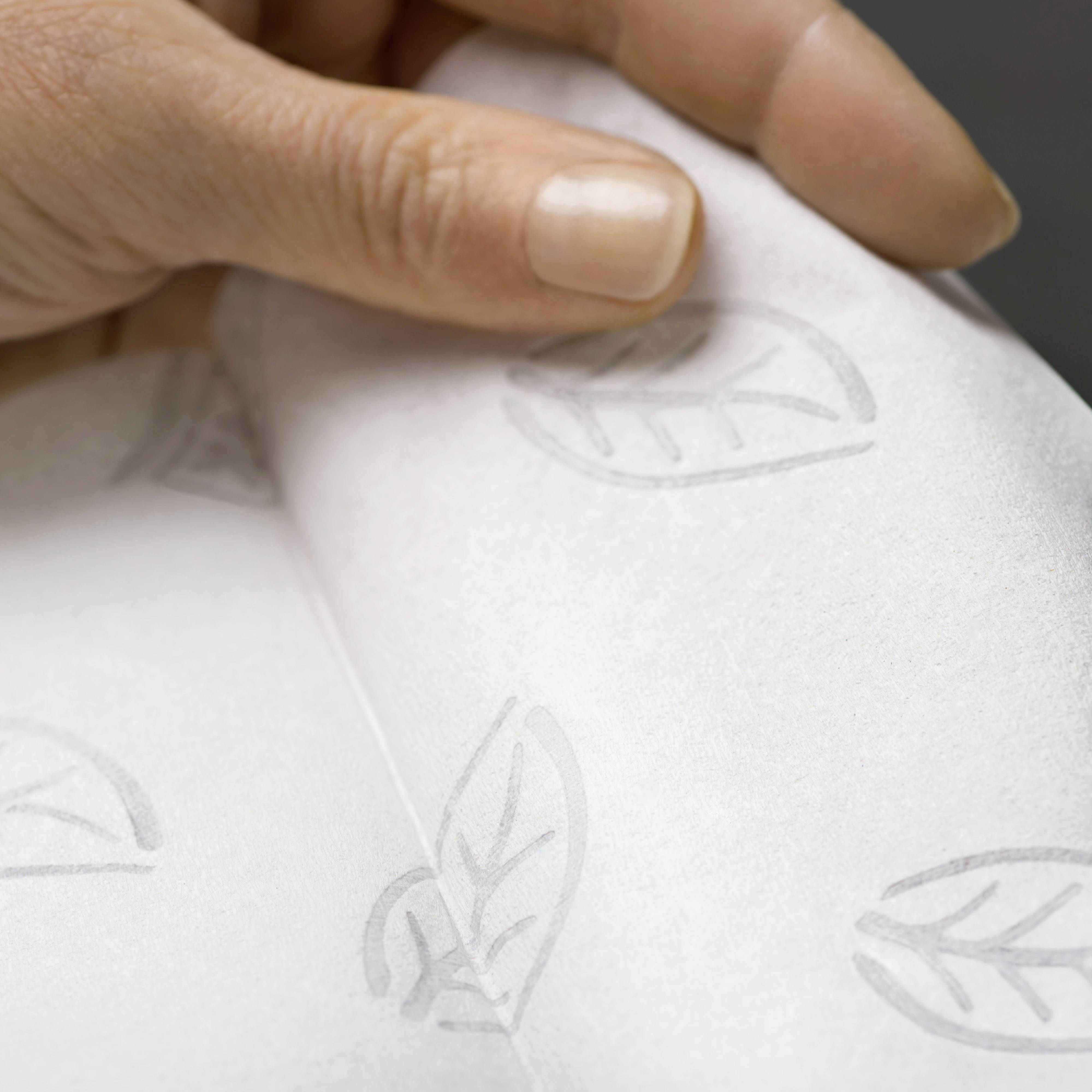 Une main tient un morceau de papier blanc avec un motif de feuille discret, suggérant un souci d'écologie.