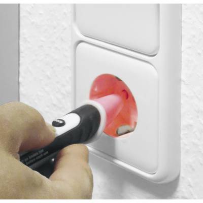 Une main teste une multiprise avec un testeur de tension. Le testeur s'illumine en rouge, indiquant la présence d'une tension électrique.