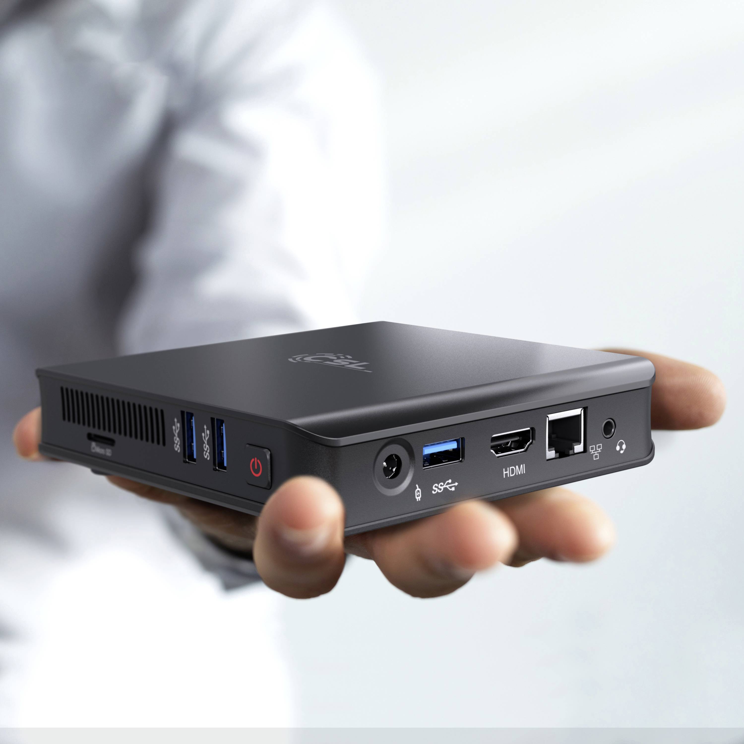 Une personne tient un petit mini-PC noir dans sa main. Le PC dispose de plusieurs ports USB, HDMI et Ethernet.