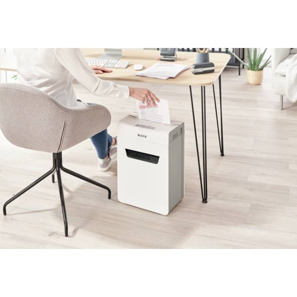 Une personne est assise à un bureau et déchiquette un document avec un destructeur de documents. La pièce est aménagée de manière moderne.