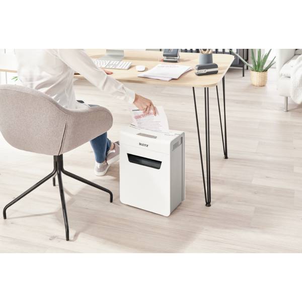 Une personne est assise au bureau et insère un document dans un destructeur de documents. Atmosphère de bureau avec un sol en bois et un mobilier moderne.