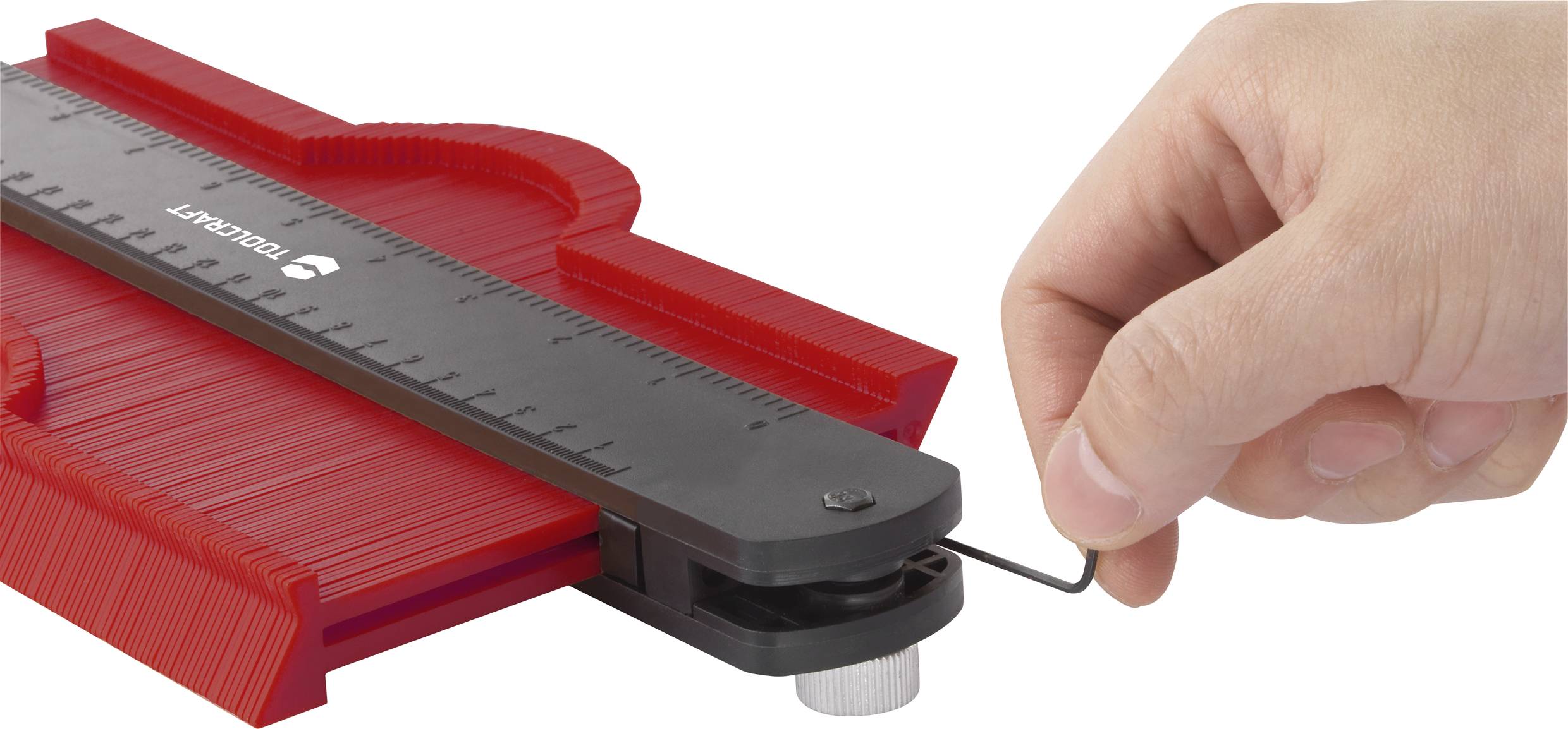 Une main dispose un calibre de contour rouge avec une règle noire pour mesurer des formes précises.