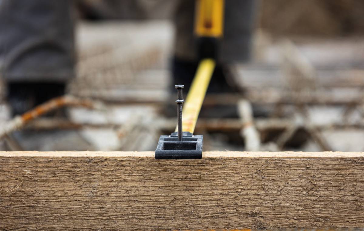 Un gros plan d'un mètre pliant fixé par un clou sur une planche en bois. Un échafaudage flou est visible en arrière-plan.
