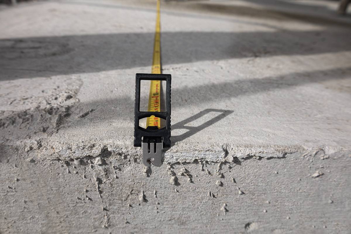 Gros plan d'un mètre ruban déroulé sur une surface en béton. L'objectif est mis au point sur le ruban de mesure projetant une longue ombre.