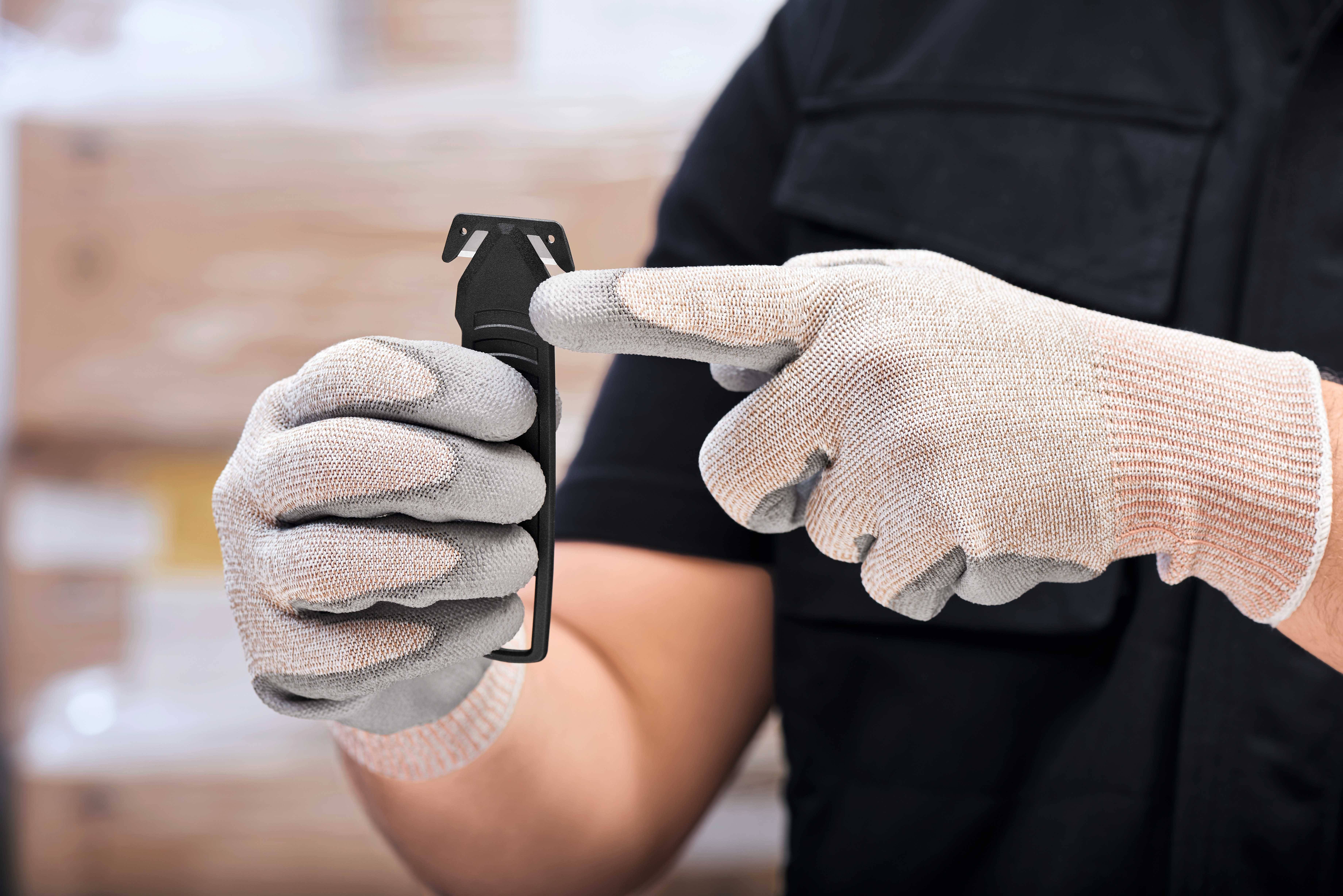 Une personne portant des gants pointe du doigt un appareil noir qu'elle tient dans sa main. L'arrière-plan est flou.