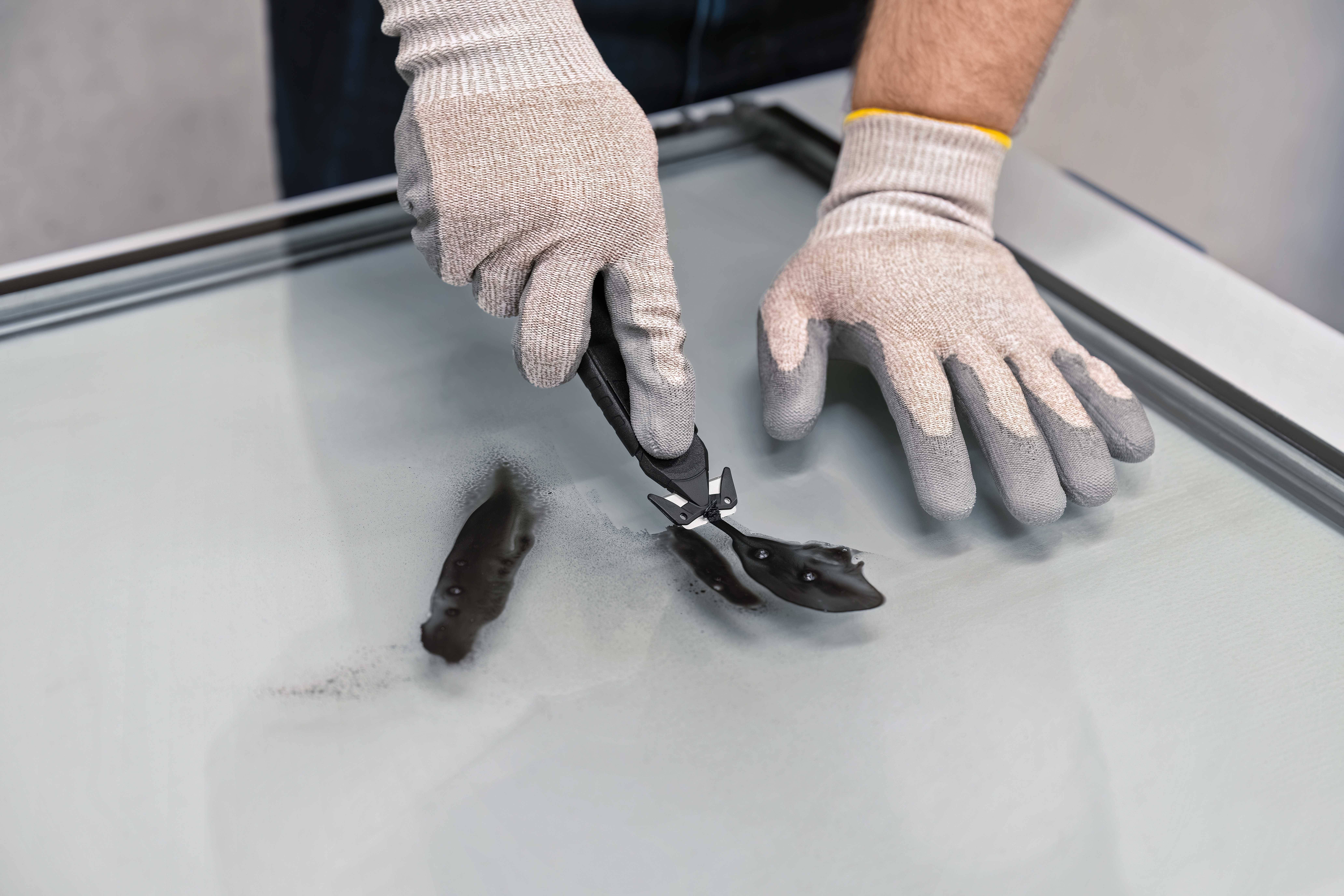 Une personne portant des gants manipule du verre à l'aide d'une pince spécialisée. La sécurité est au premier plan lors du traitement soigneux du verre.