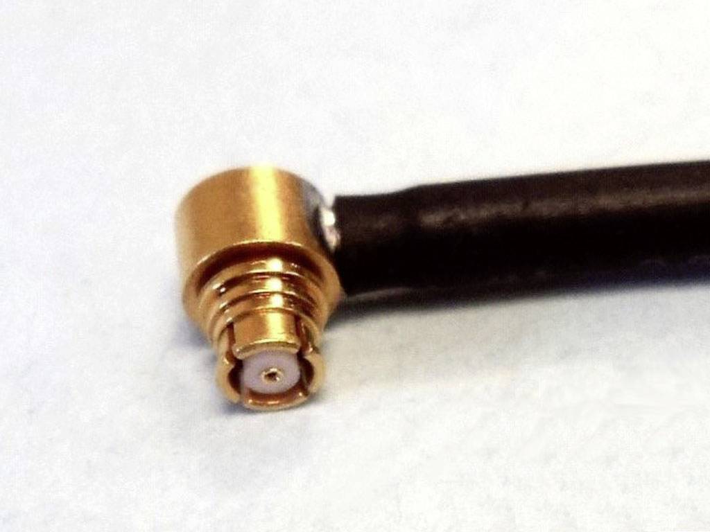 Un connecteur coaxial doré avec un raccordement coudé est fixé à un câble noir.