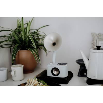 Une table blanche avec une plante d'intérieur, deux tasses, un pichet blanc et un haut-parleur moderne de style rétro.