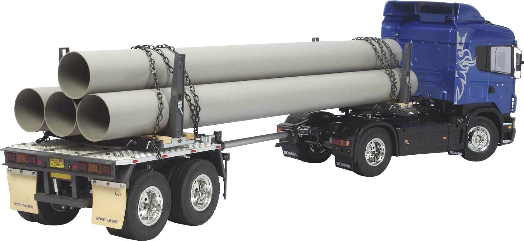 Camion bleu avec remorque transportant de grands tuyaux gris sécurisés par des chaînes. Le camion est sur un fond blanc.